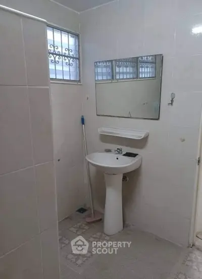 Simple bathroom with pedestal sink and wall mirror in a tiled setting.