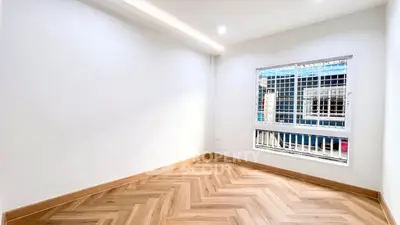 Spacious empty room with elegant herringbone wooden flooring and large window.