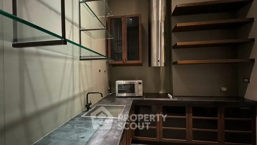 Modern kitchen with sleek countertops and open shelving, featuring a microwave and stainless steel range hood.