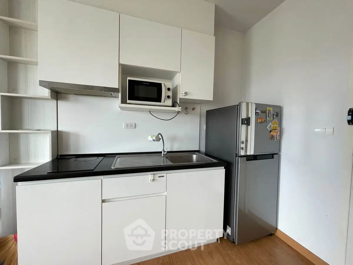 Modern kitchen with sleek cabinetry, microwave, and stainless steel fridge in a compact layout.