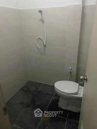Compact bathroom with tiled walls and floor, featuring a toilet and showerhead.