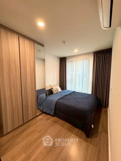 Cozy modern bedroom with wooden flooring and large window for natural light.