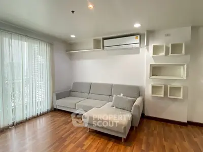 Modern living room with sleek grey sofa and wooden flooring, featuring stylish wall shelves and air conditioning.