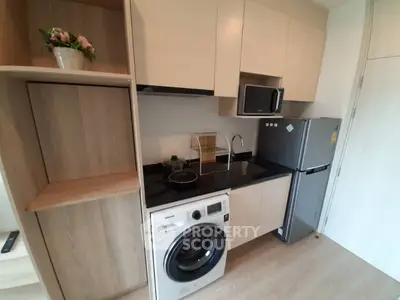Modern compact kitchen with washing machine, microwave, and fridge in stylish apartment.