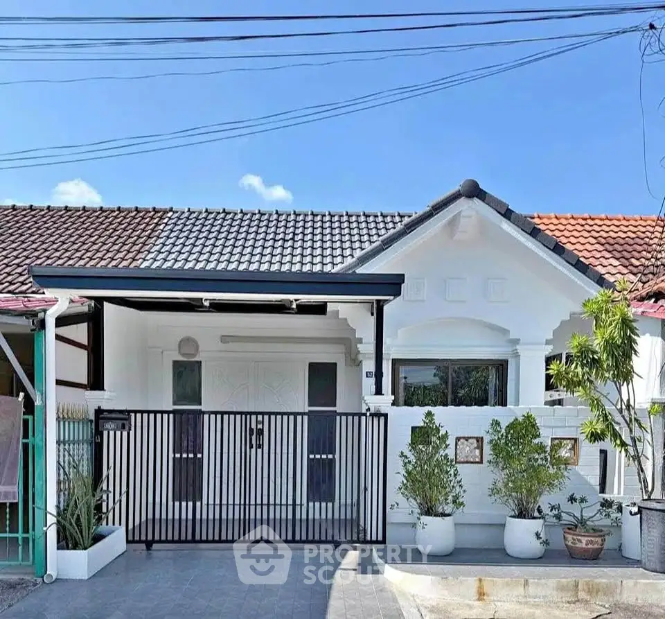Charming single-story home with modern gate and lush potted plants, perfect for cozy living.