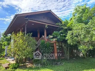 Charming elevated wooden house with lush garden and tropical trees, perfect for serene living.