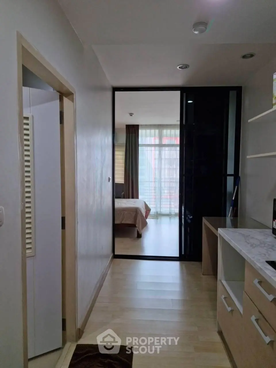 Modern apartment hallway leading to a cozy bedroom with natural light and sleek furnishings.