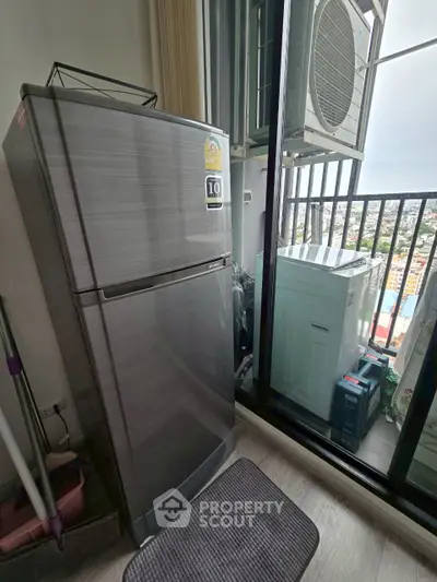 Compact balcony with city view, featuring a refrigerator and air conditioning unit.