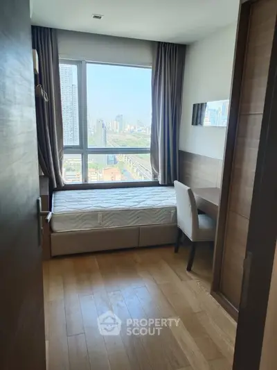 Cozy bedroom with city view, wooden flooring, and study desk in modern apartment.