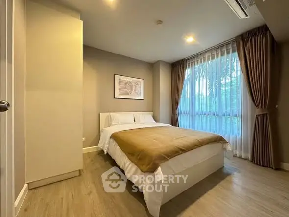 Cozy bedroom with modern decor and large window offering natural light.