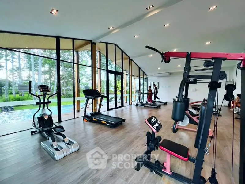 Modern gym with large windows overlooking a pool and lush greenery