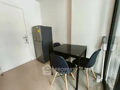Modern dining area with sleek black table and chairs, adjacent to a compact refrigerator.