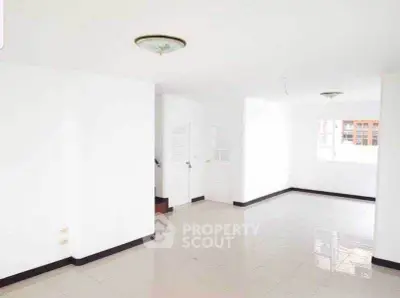 Spacious white-walled living room with tiled flooring and ample natural light.