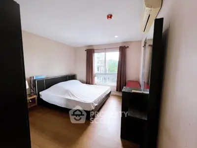 Spacious bedroom with large window and wooden flooring in modern apartment.