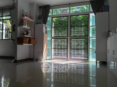 Spacious living room with large windows and modern decor, offering abundant natural light and a serene garden view.