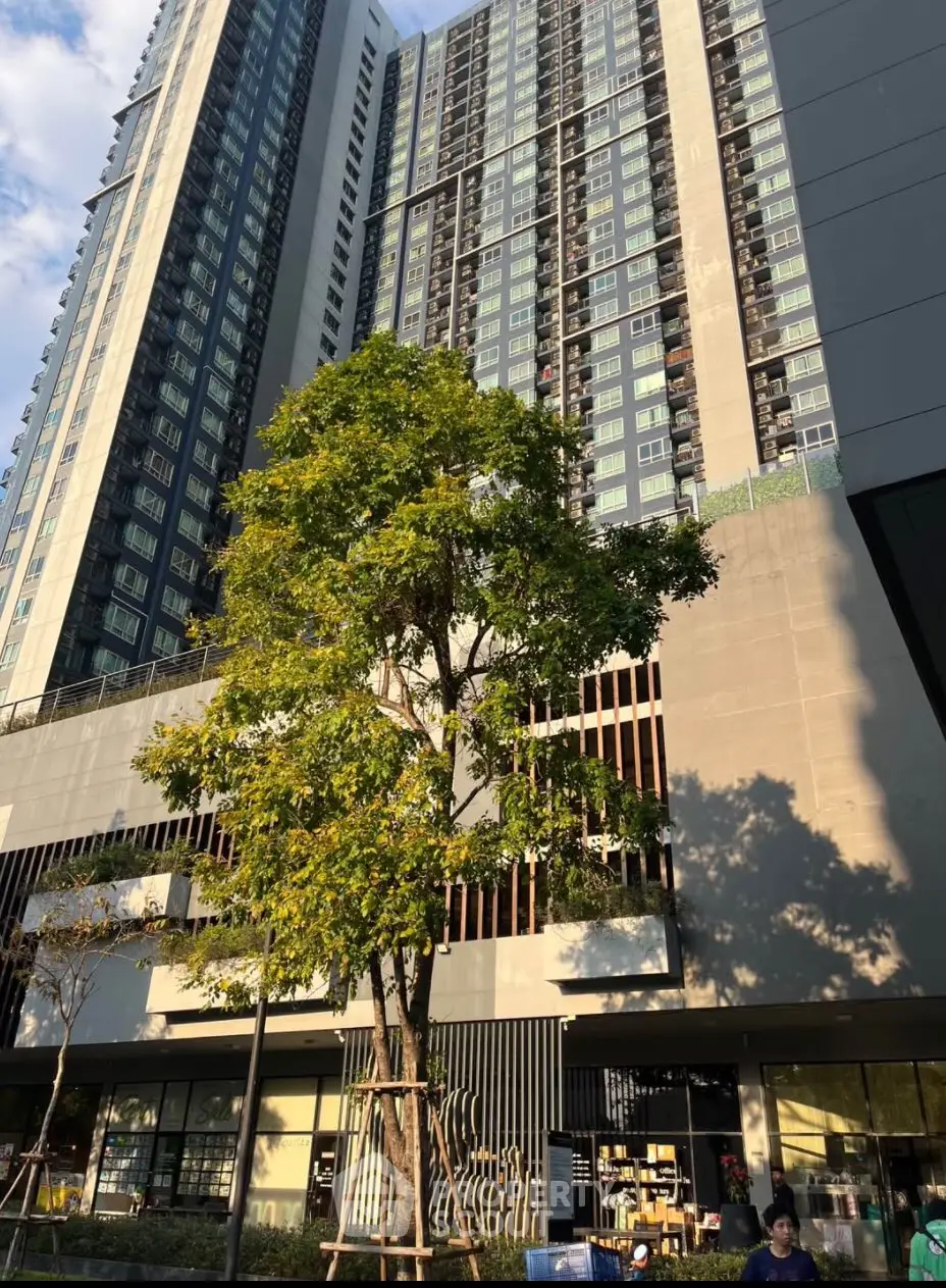 Modern high-rise building with lush greenery and retail spaces at the base.