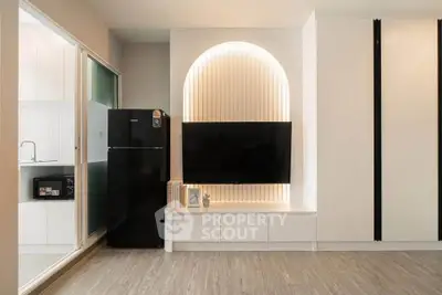 Modern living room with sleek TV setup and stylish lighting, adjacent to a compact kitchen area.