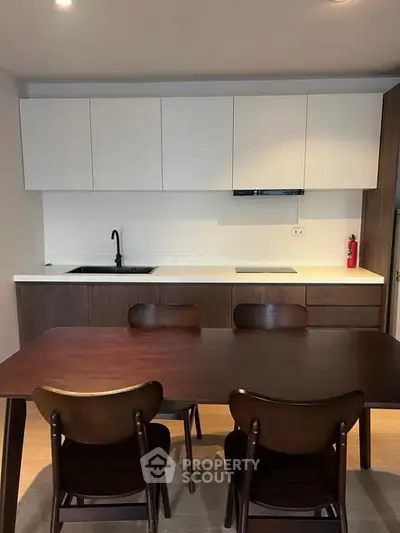 Modern kitchen with sleek cabinetry and dining area, featuring a dark wood table and chairs.