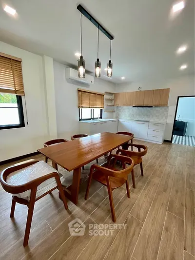 Modern dining area with wooden table and chairs, open kitchen layout, and stylish lighting.