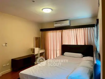 Spacious bedroom with modern furnishings and natural light from large window.