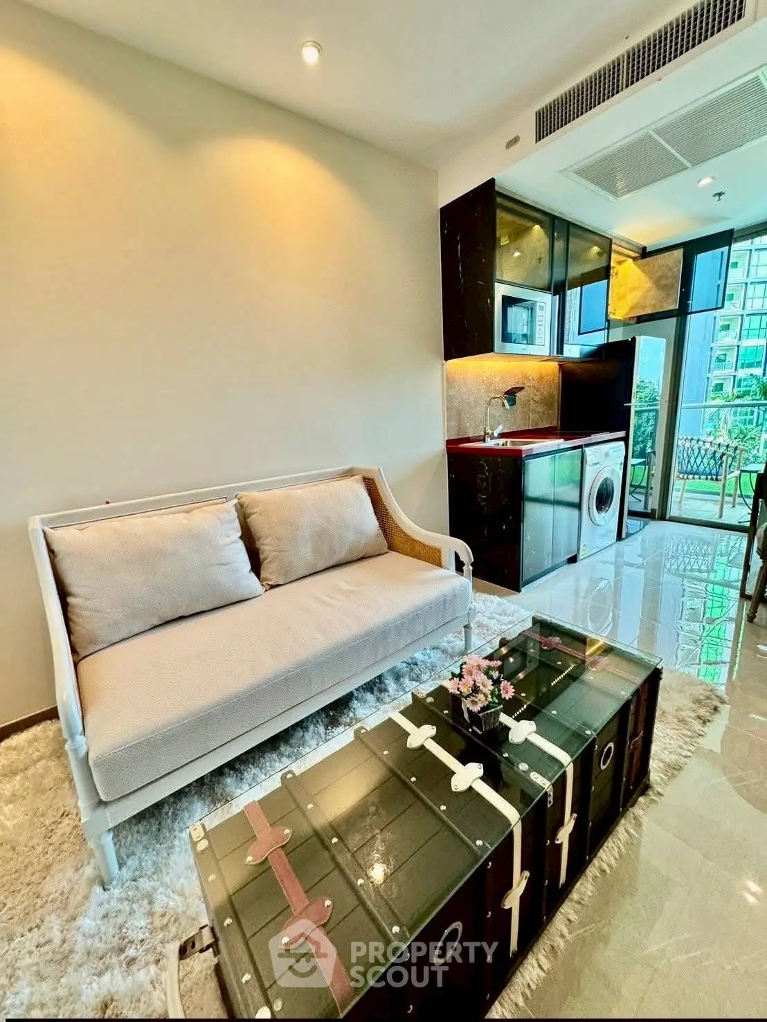 Modern living room with stylish furniture and open kitchen layout, featuring a washing machine and large windows.