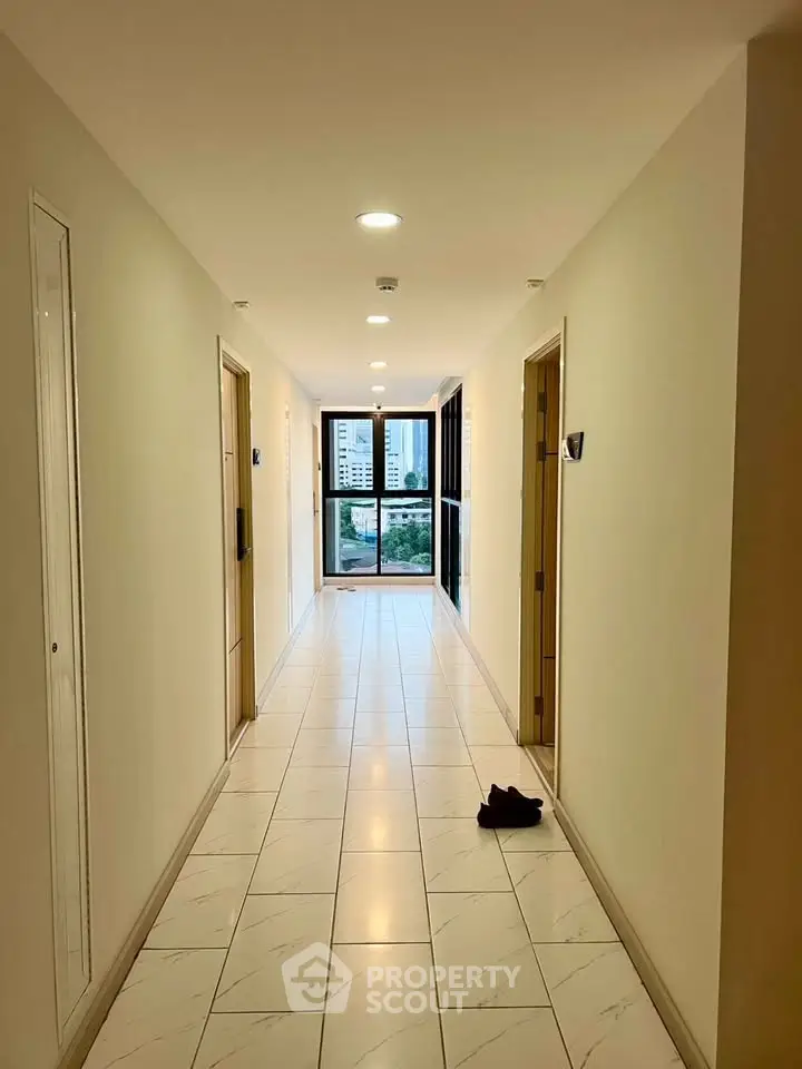 Bright corridor with tiled flooring leading to a window with city view in modern building.