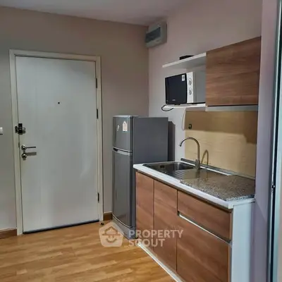 Modern compact kitchen with wooden cabinets and stainless steel appliances in a cozy apartment.