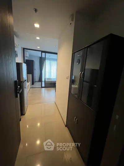 Modern apartment hallway leading to a bright living area with sleek furniture and large windows.