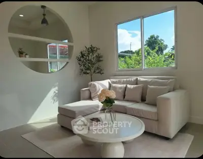 Charming living room with cozy sofa and large window offering lush garden view.
