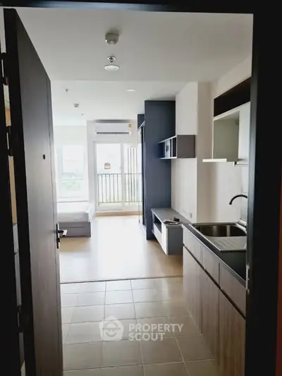 Modern apartment interior with open kitchen and bright living area leading to balcony.