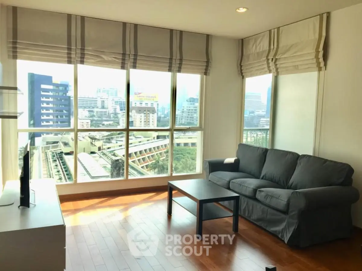 Spacious living room with large windows offering stunning city views, featuring cozy seating and elegant decor.