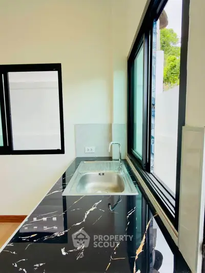 Modern kitchen with sleek black marble countertop and large windows for natural light.