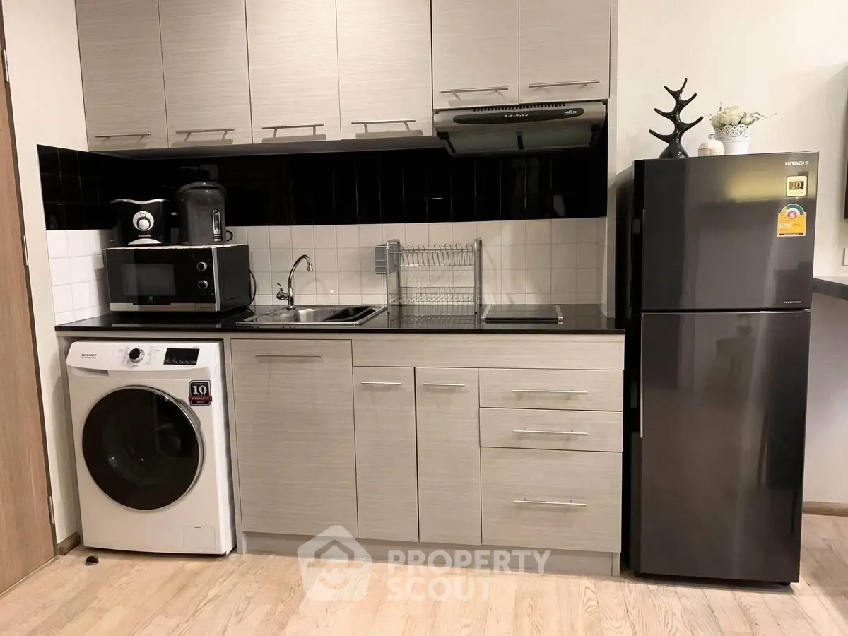 Modern kitchen with sleek cabinets, washing machine, and fridge in compact layout.