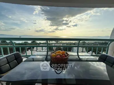 Stunning balcony view with glass table overlooking ocean sunset, perfect for relaxation.