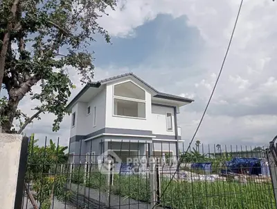 Modern two-story house with large windows and a fenced yard, surrounded by greenery and open sky.