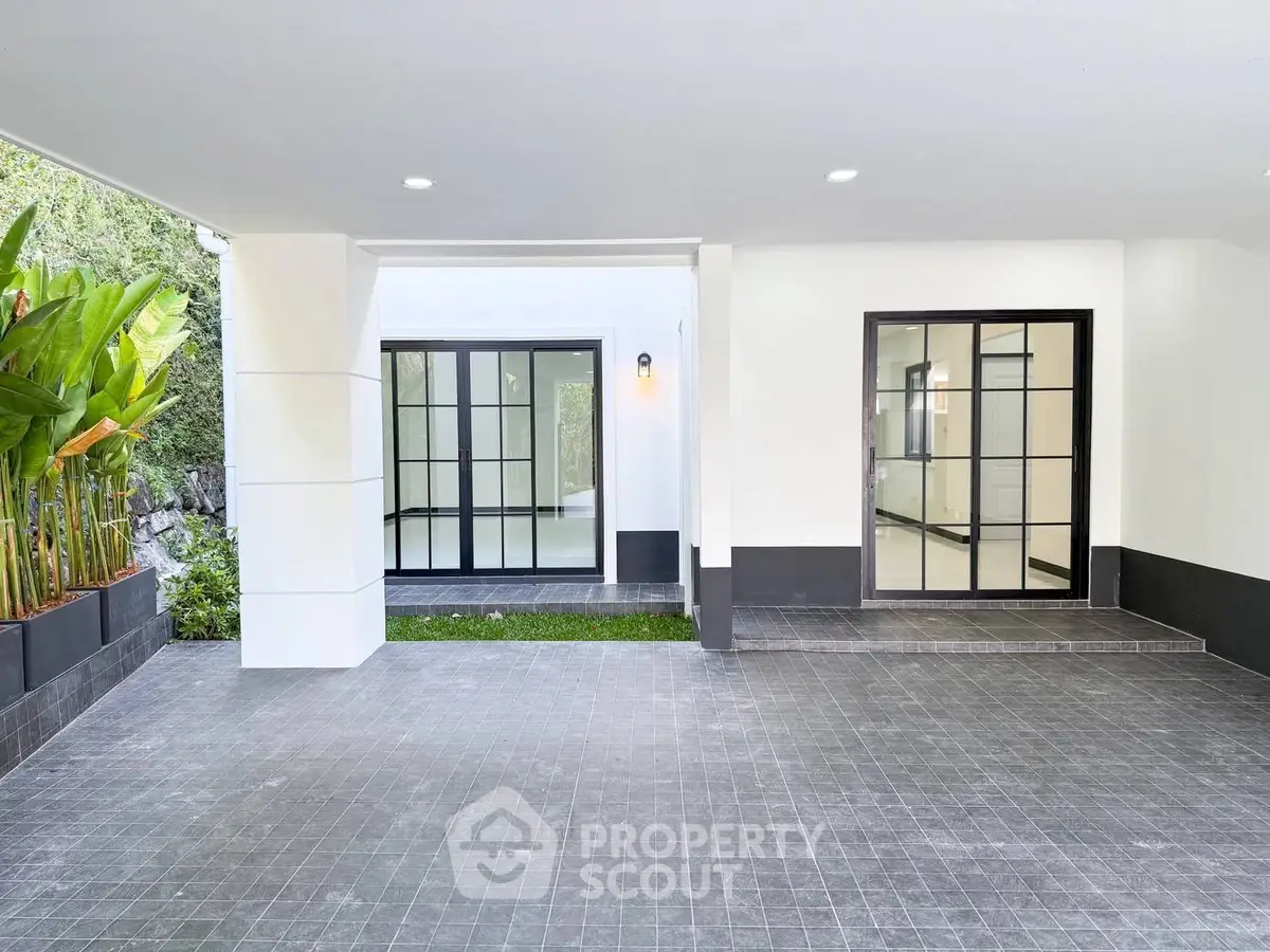 Modern home entrance with sleek black-framed glass doors and lush greenery