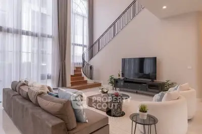Luxurious living room with high ceilings, elegant staircase, and modern decor.