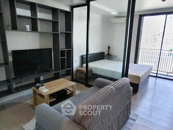 Modern studio apartment with open layout, featuring a cozy living area and a comfortable bedroom separated by glass partitions.