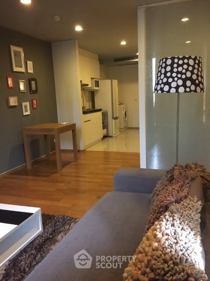 Modern living room with cozy sofa, stylish lamp, and compact kitchen area featuring washing machine.