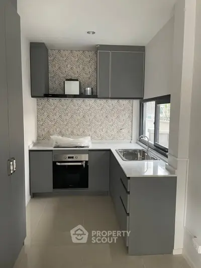 Modern kitchen with sleek grey cabinets and built-in oven, featuring a stylish backsplash and ample natural light.