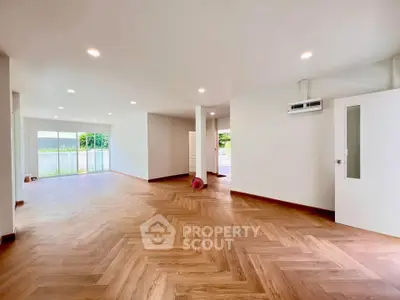 Spacious open-plan living area with wooden flooring and large windows offering natural light.