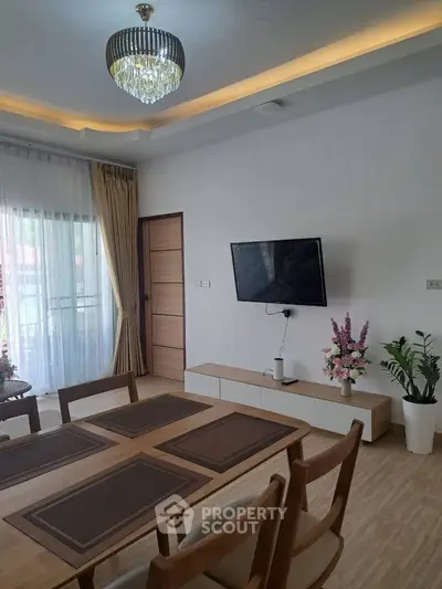 Elegant dining area with modern decor and wall-mounted TV, featuring a chic chandelier and large window.