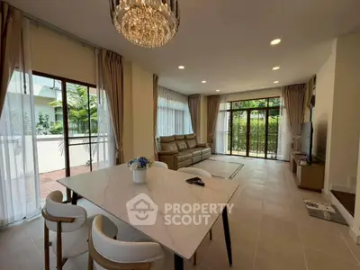 Spacious living room with elegant chandelier and garden view, featuring modern furniture and large windows.