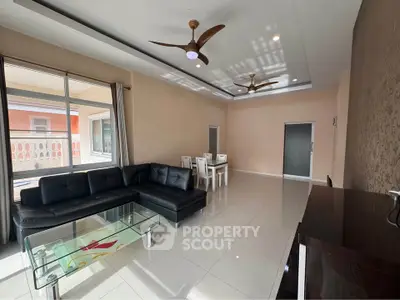 Spacious modern living room with sleek black leather sofa and elegant dining area, featuring ceiling fans and large windows.