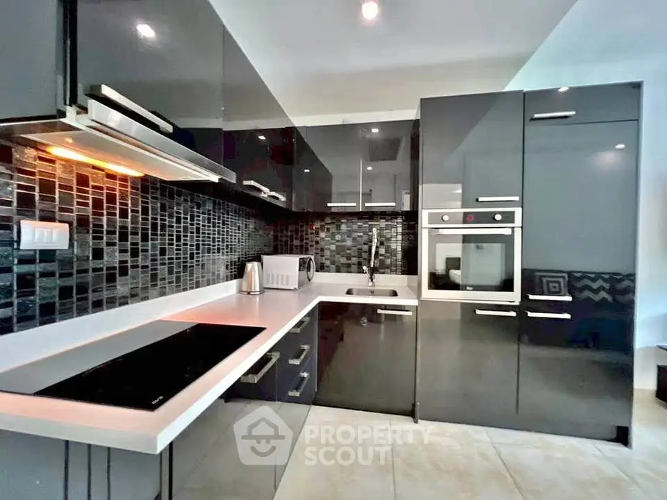 Modern kitchen with sleek black cabinetry and built-in appliances, featuring a stylish backsplash.