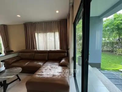 Spacious living room with large leather sofa and garden view through sliding glass doors.