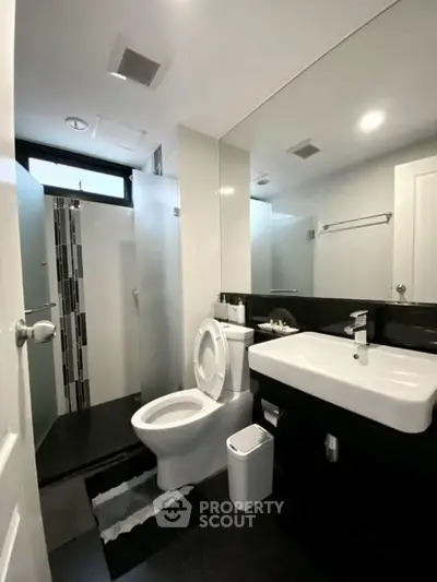 Modern bathroom with sleek black and white design, featuring a spacious shower and contemporary fixtures.