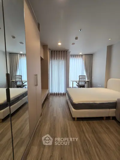 Modern bedroom with wooden flooring and large windows for natural light.