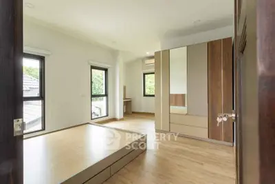 Spacious bedroom with wooden flooring and large windows offering natural light.