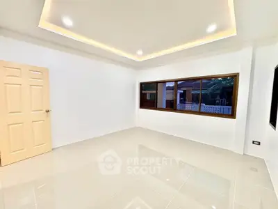 Spacious empty room with modern ceiling lights and large window, perfect for customization.